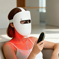 Woman using a white Apollo SG LED face mask with a black controller for red light therapy in a modern room.