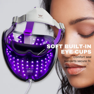 A close-up of a woman's face next to a wearable WAVLO Apollo SG LED light therapy mask. The mask is illuminated with purple light and has built-in eye cups, with text reading 'SOFT BUILT-IN EYE CUPS' and 'Comfort seal supports secure fit.