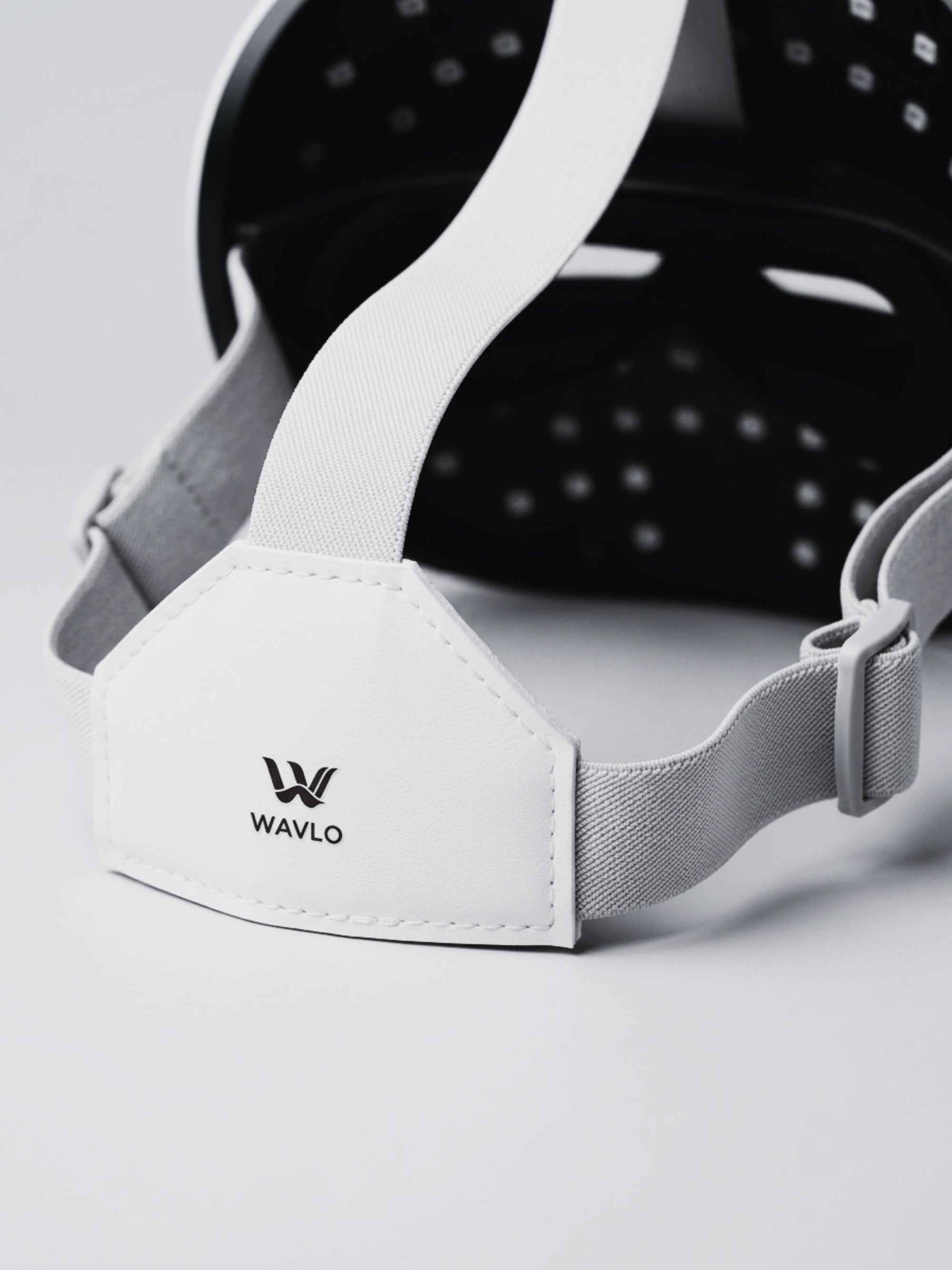 Close-up of a white adjustable wearable device with an adjustable strap and a visible WAVLO logo on the front tab, photographed on a clean light gray background.